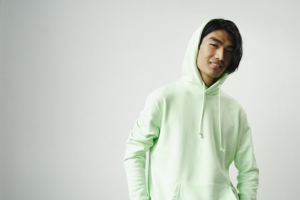 Casual portrait of a smiling Asian man wearing a light green hoodie on a white background.